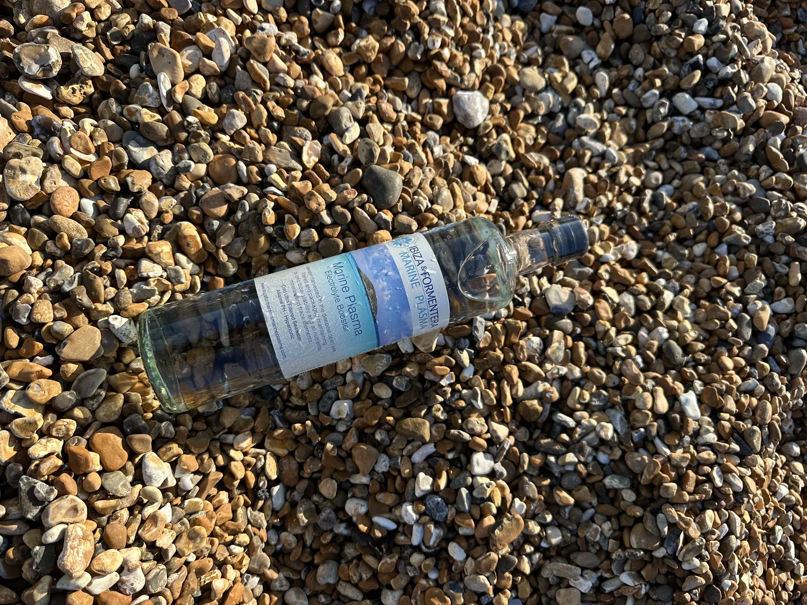 Ibiza & Formentera Marine Plasma electrolyte booster bottle on a pebble beach